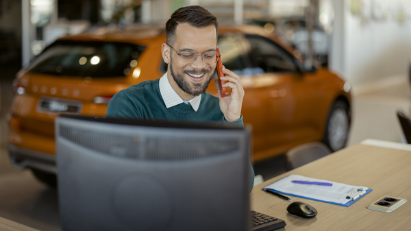 Salesperson talking on phone at desk inside car dealership