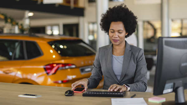 Saleswoman at desk inside dealership, typing on computer